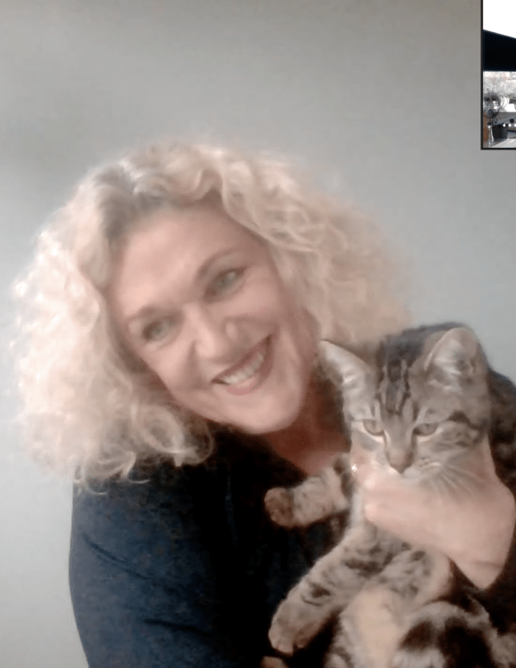 Mirjam Kaijer glimlacht, zij draagt een zwart trui en houdt een getijgerde kat vast. Haar blonde krullen lichten op door daglicht van een raam aan de zijkant. Inzet podcasthost Jolanda Gooiker